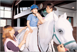 Clients on a pony with therapist, adjusting helmet
