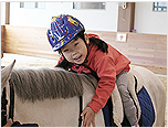 재활승마 참가아동이 말 위에서 양팔로 말을 안아주는 모습